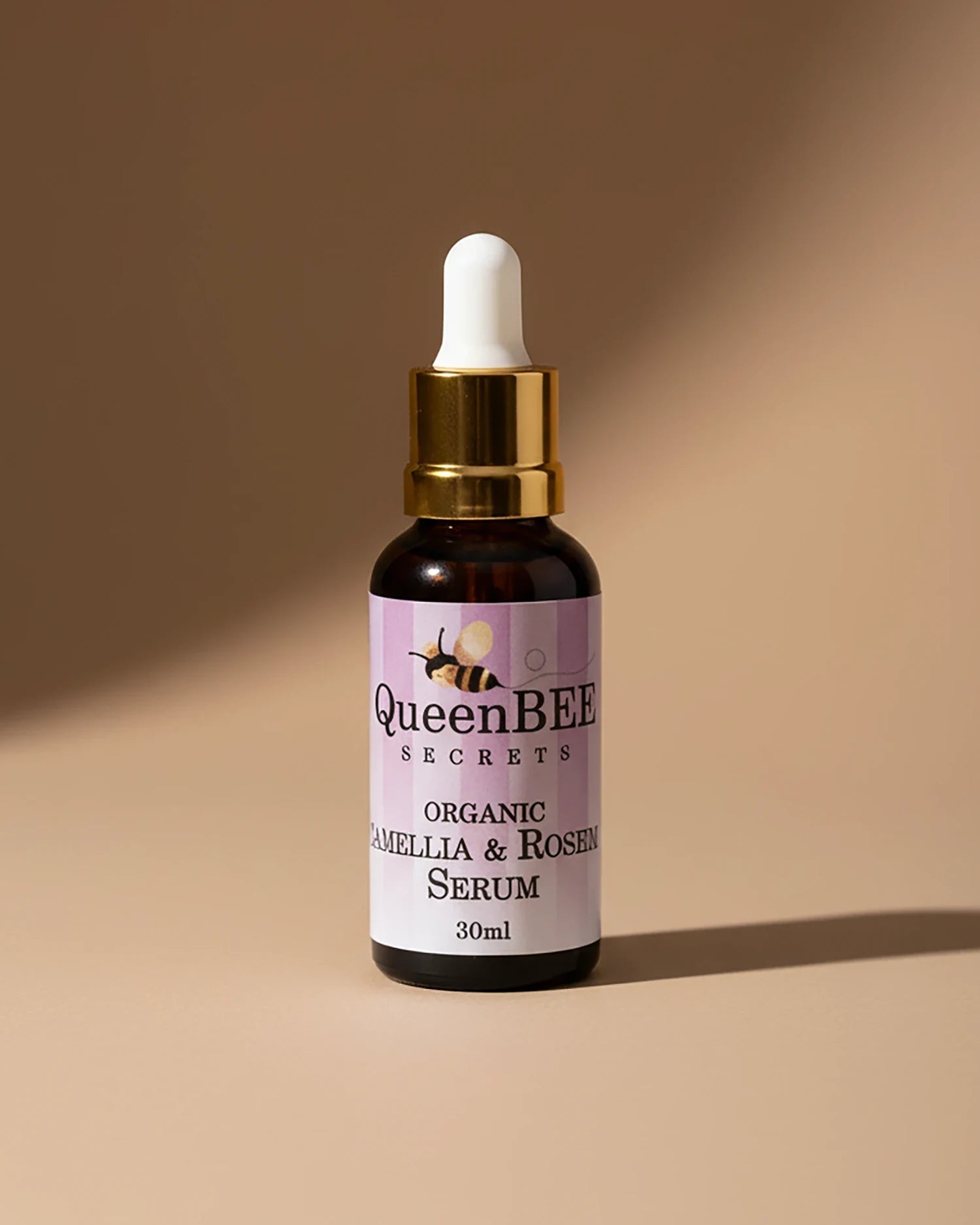 QueenBEE Secrets organic camelilla & rosehip serum bottle on a beige background