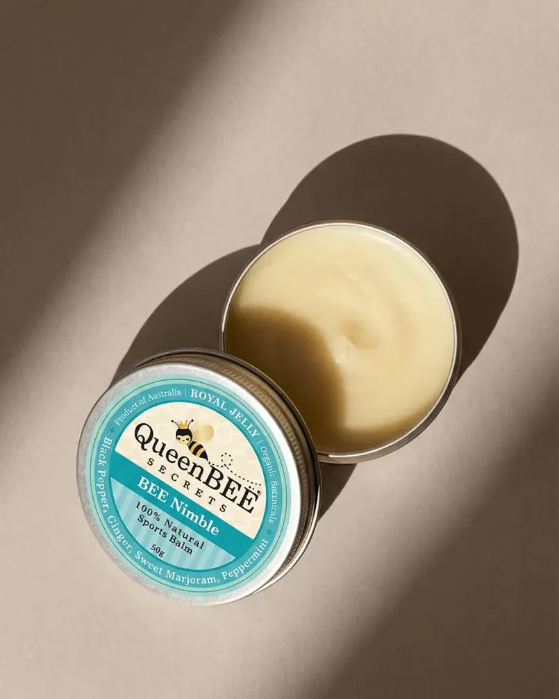 Open tin of QueenBEE Bee Nimble balm on a beige background