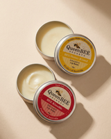 Two tins of Queen Bee Secrets lip balm on a beige background