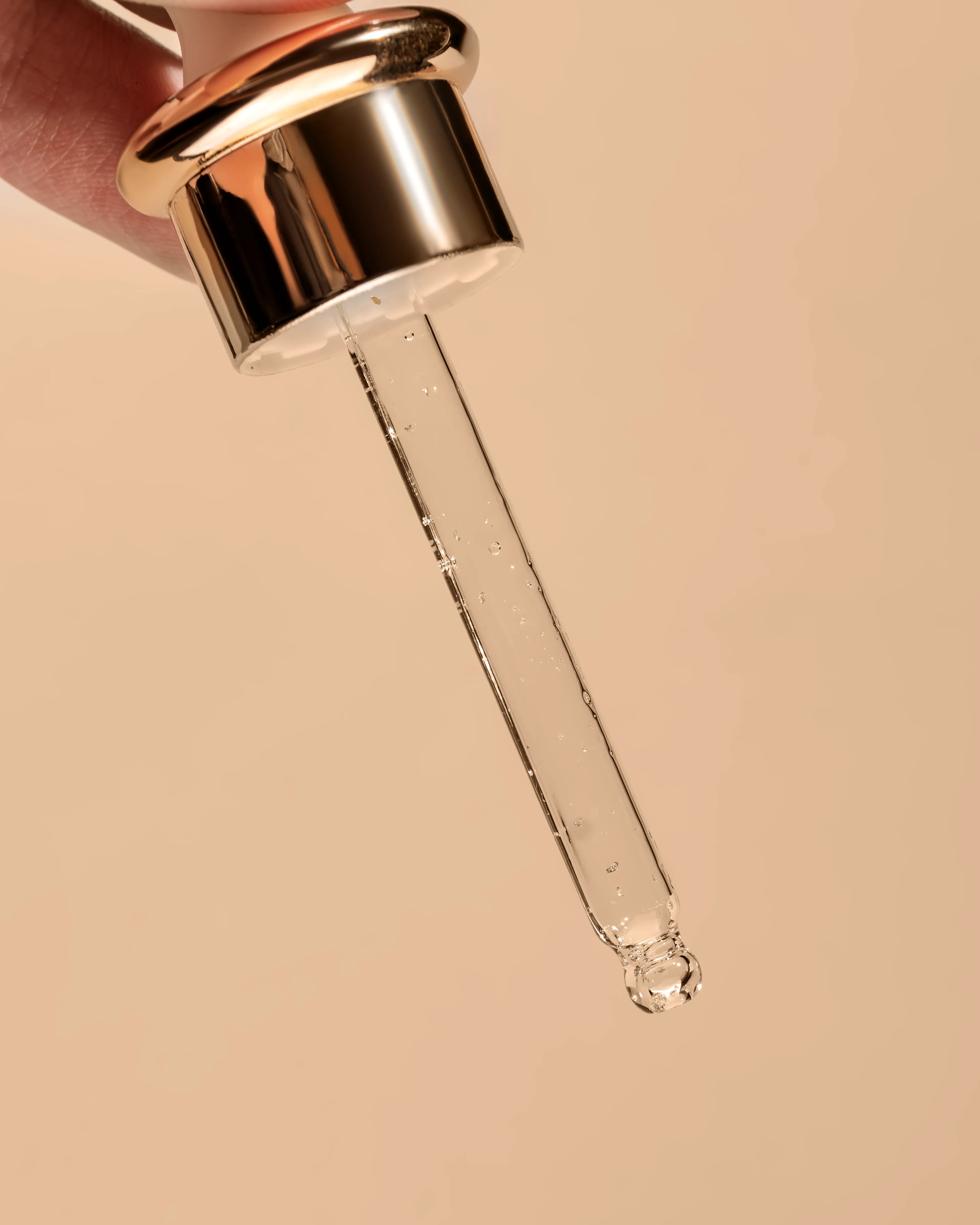Gold and clear dropper with a drop of liquid on a beige background